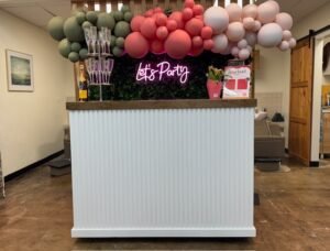 Front view of our handcrafted bar styled with a lush green backdrop and vibrant neon 'Let’s Party' sign—modern, eye-catching, and perfect for photo-worthy moments at any event.